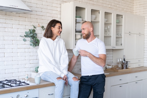 Young couple husband with wife at home in the kitchen, happy smile laugh, drink coffee in the morning