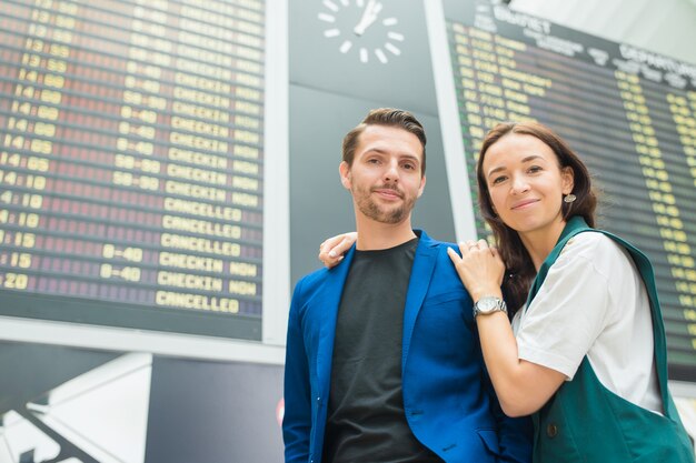 フライト情報ボードを見て国際空港で若いカップル