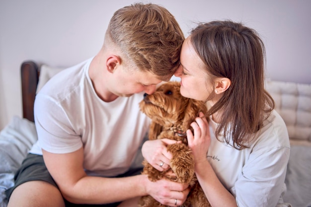 Foto una giovane coppia tiene un cane cockapoo tra le braccia sul letto.