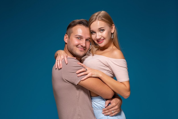 Young couple is hugging on blue background in studio. They wear T-shirts, jeans and smile. Friendship, love and relationships concept