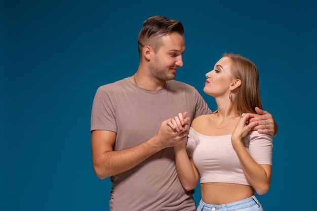 Young couple is hugging on blue background in studio. They wear T-shirts, jeans and smile.