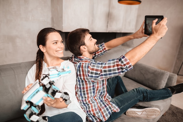 Young couple is sitting on couch and doing selfie.