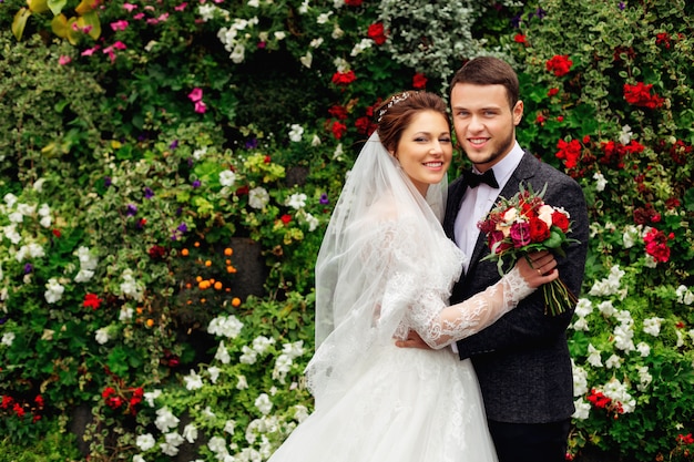 The young couple is standing on the background of the flower garden