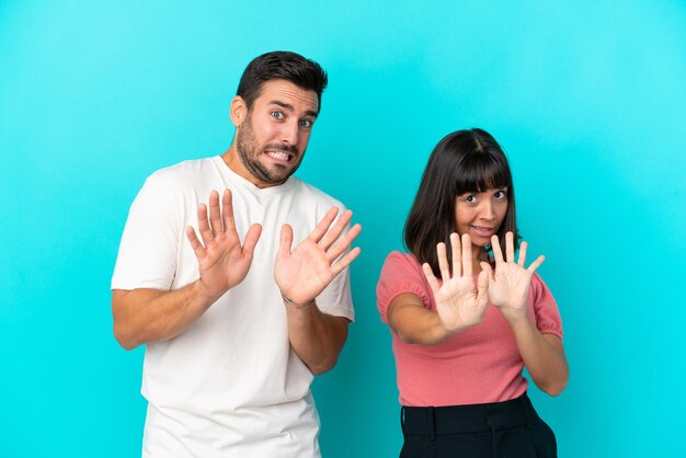 Young couple isolated on blue background is a little bit nervous and scared stretching hands to the front