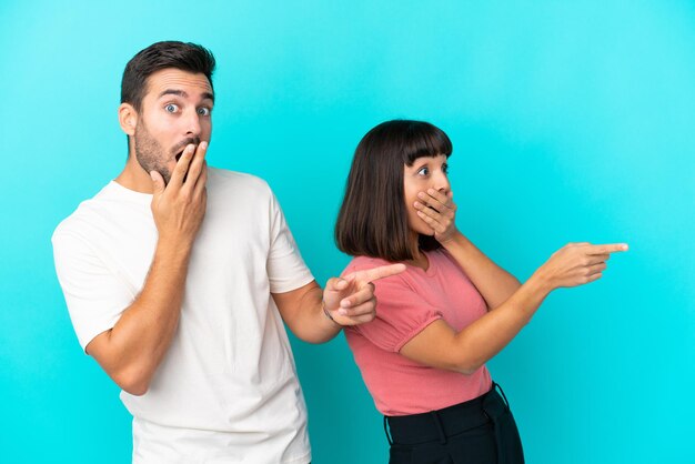 Foto giovane coppia isolata su sfondo blu che punta il dito di lato con una faccia sorpresa