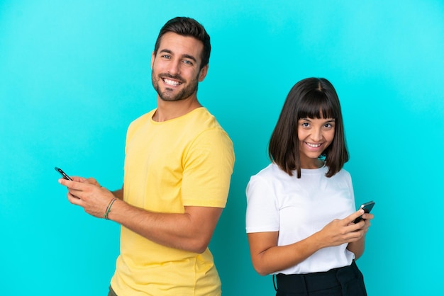 Young couple isolated on blue background sending a message or email with the mobile