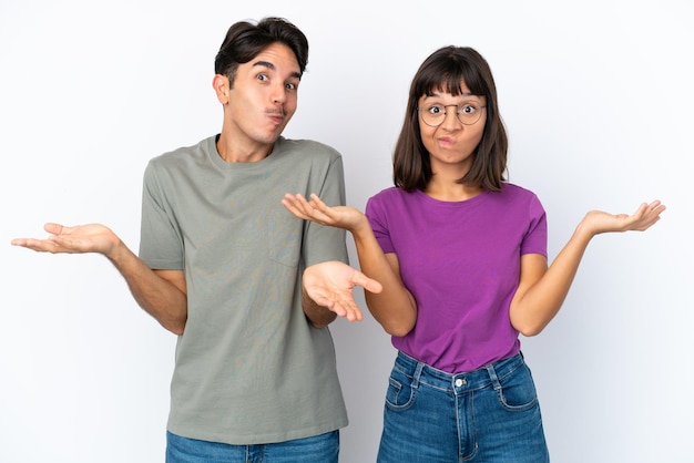 Young couple isolated on isolated white background having doubts while raising hands and shoulders