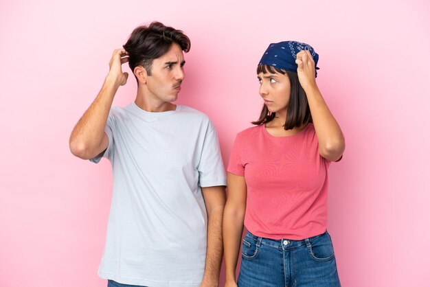 Young couple isolated on pink background having doubts while scratching head