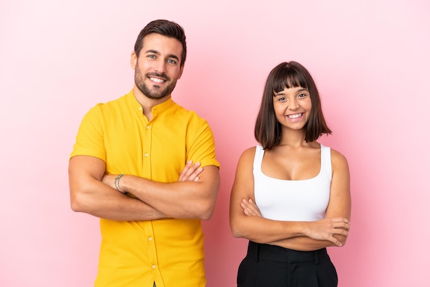 Young couple isolated on pink background keeping the arms crossed in frontal position