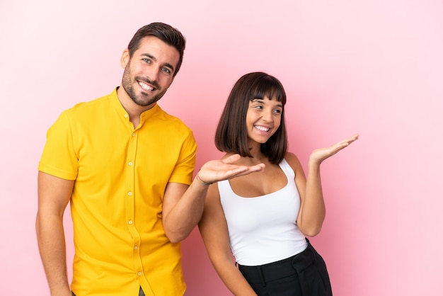 Young couple isolated on pink background pointing back and presenting a product