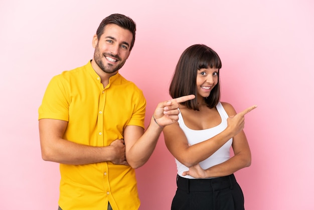 Young couple isolated on pink background pointing finger to the side in lateral position