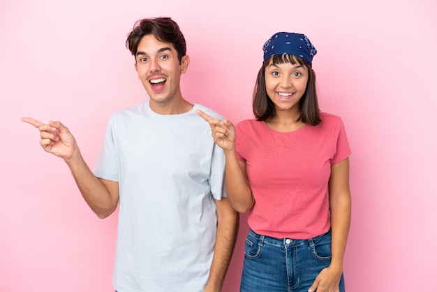 Молодая пара изолирована на розовом фоне, указывая пальцем в сторону и представляя продукт