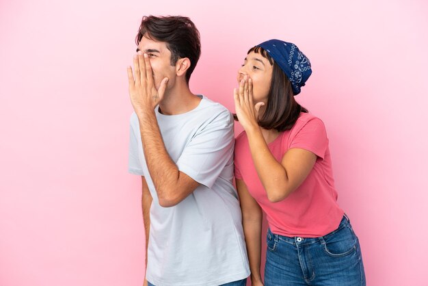 Young couple isolated on pink background shouting with mouth wide open to the lateral