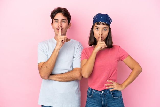 Young couple isolated on pink background showing a sign of closing mouth and silence gesture