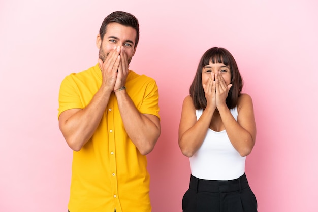 Young couple isolated on pink background smiling a lot while covering mouth