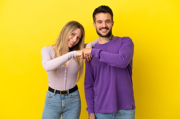 Молодая пара на изолированном желтом фоне, стуча кулаками