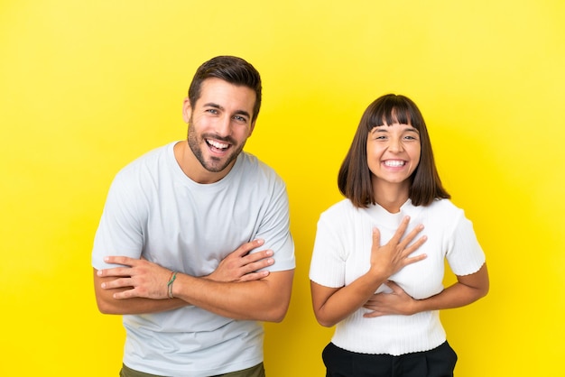 Young couple isolated on yellow background keeping the arms crossed while smiling