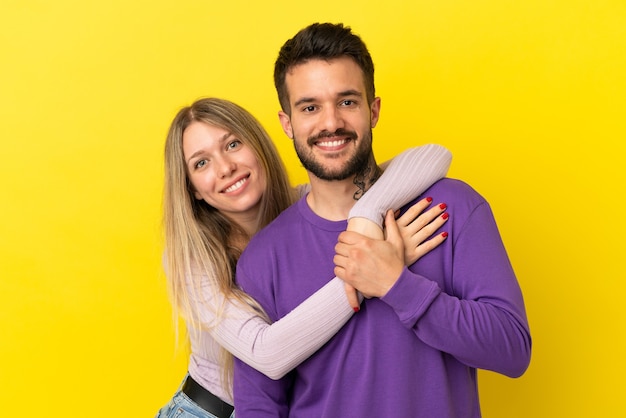 Young couple over isolated yellow background laughing and hugging