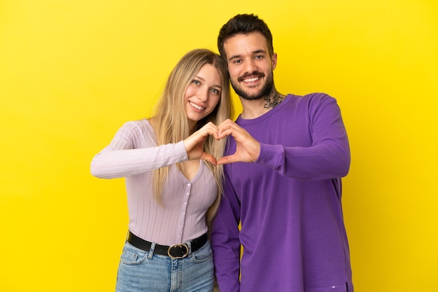 Young couple over isolated yellow background making a heart with hands