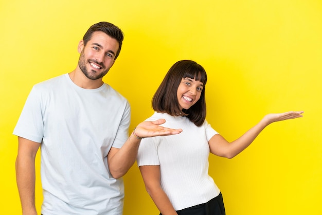 Young couple isolated on yellow background pointing back and presenting a product