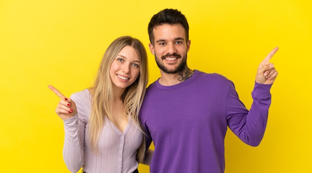 Young couple over isolated yellow background pointing finger to both sides