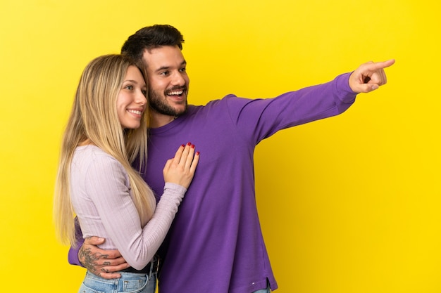 Young couple over isolated yellow background pointing finger to the side and presenting a product