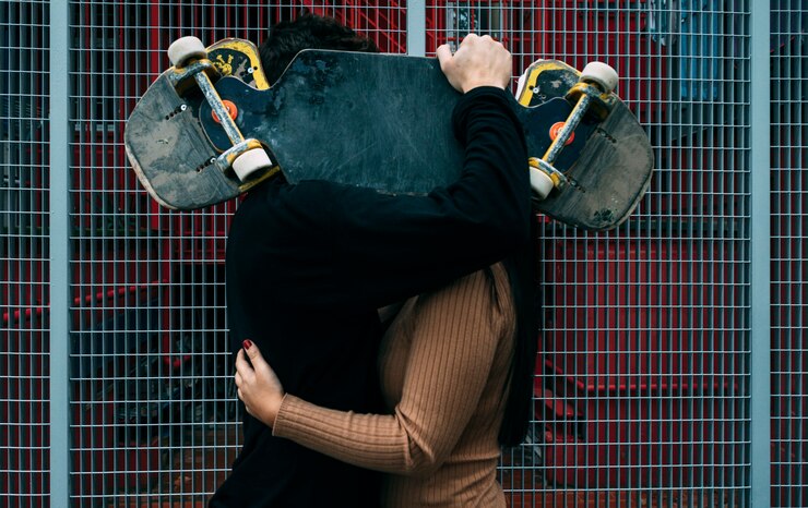 Photo young couple kiss hiding behind skateboard. love concept. urban sport concept.