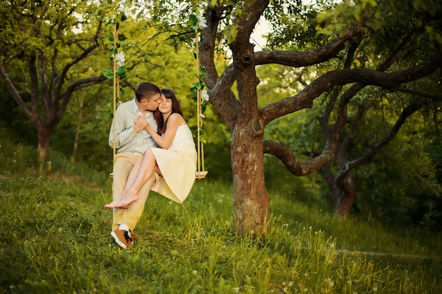 A young couple kiss in park on tree swing