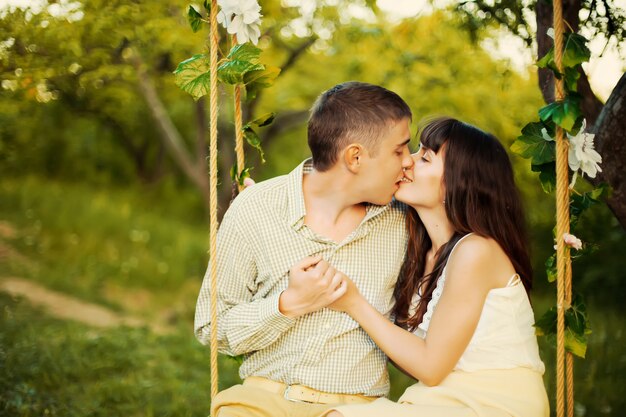 Молодая пара целуется в парке на качелях