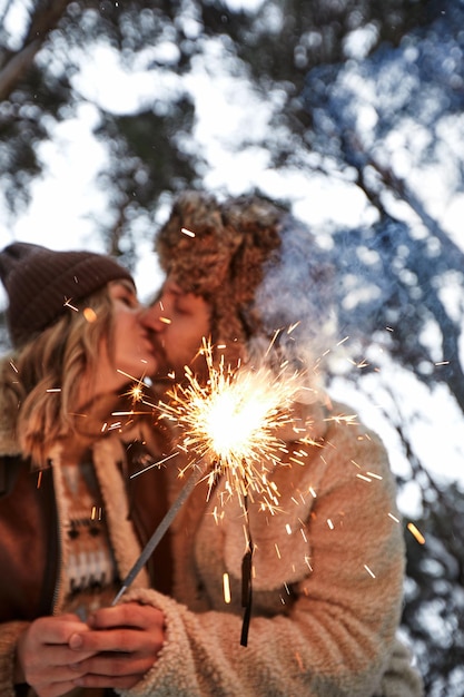 Young couple kissing and holding sparklers on a background of snowcovered park and trees loving couple smiles on their faces magical winter on the eve of Valentine's Day