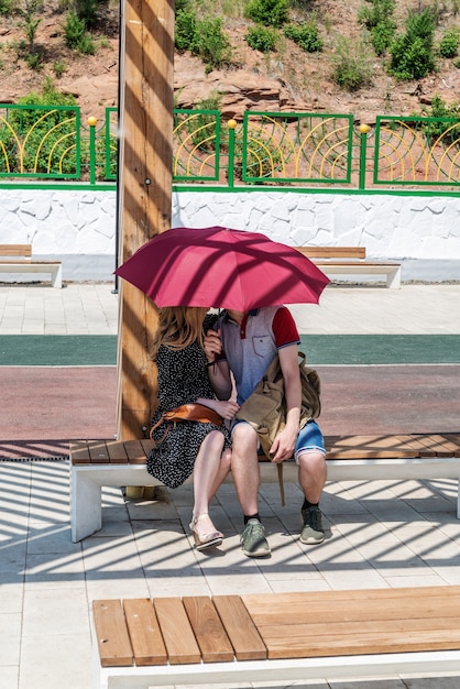 Young couple kissing under umbrella while sitting on a bench