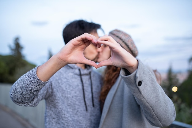 Giovani coppie che si baciano mentre formano un cuore romantico con le loro mani valentine39s day