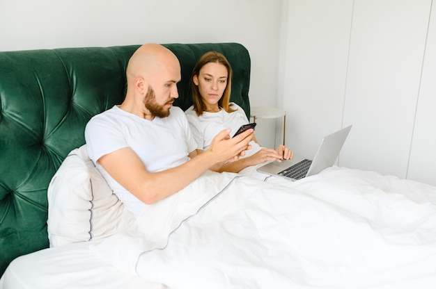 Young couple lie in bed with phones