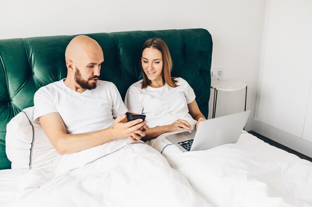 Young couple lie in bed with phones