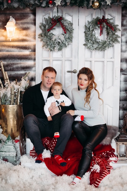 Young couple and little cute son sitting together near white door, looking at front and posing