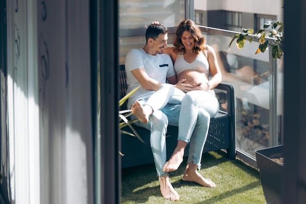 Молодая пара смотрит на свой беременный живот счастливой и улыбающейся