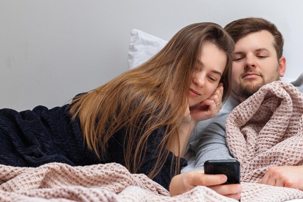 Young couple looking at smartphone while lying on the bed in the bedroom