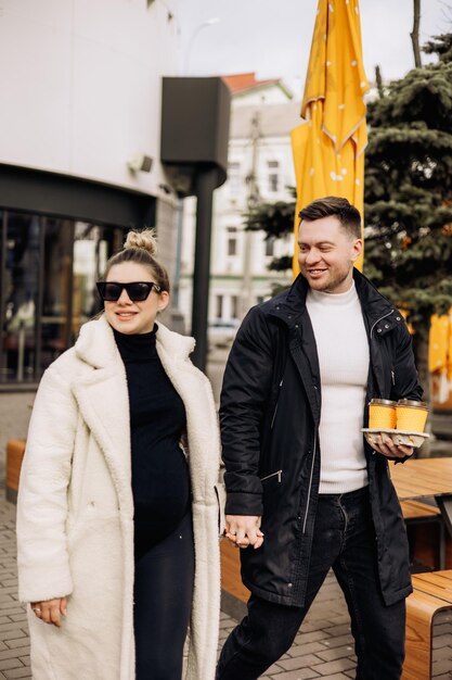 A young couple in love in autumn in outerwear walks on the street and drinks coffee Recreation in the open air Young stylish couple