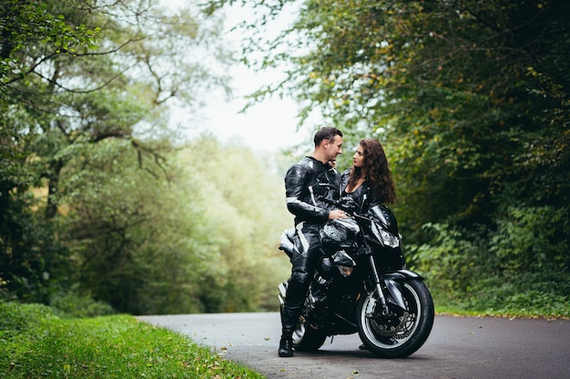 Young couple in love in black leather clothes near a black sports motorcycle on the road