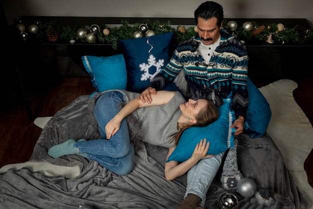 Young couple in love embraced in their living room on a Christmas night lying with pillows.