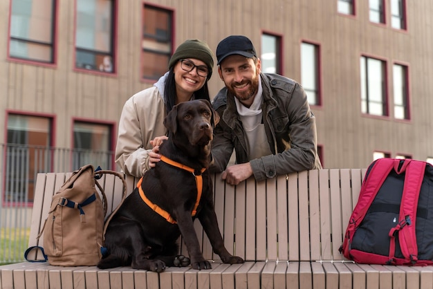 Young couple in love enjoying with their adorable Labrador dog while walking at the street and posing to the camera Pet sitting at the bench