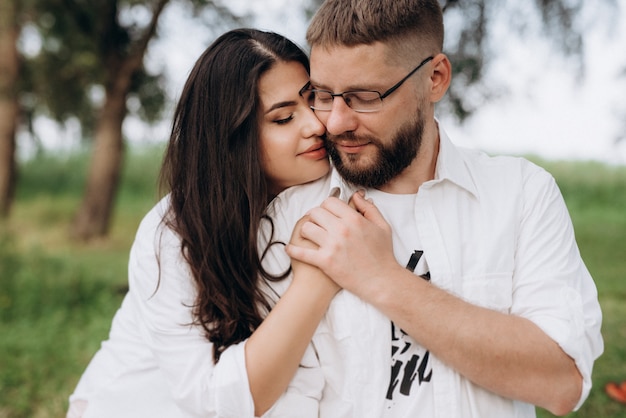 Young couple in love a guy with a beard and a girl with dark hair in light clothes in the green forest