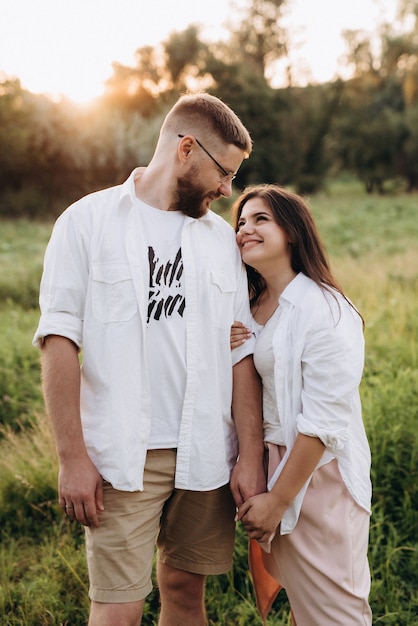 Young couple in love a guy with a beard and a girl with dark hair in light clothes in the green forest