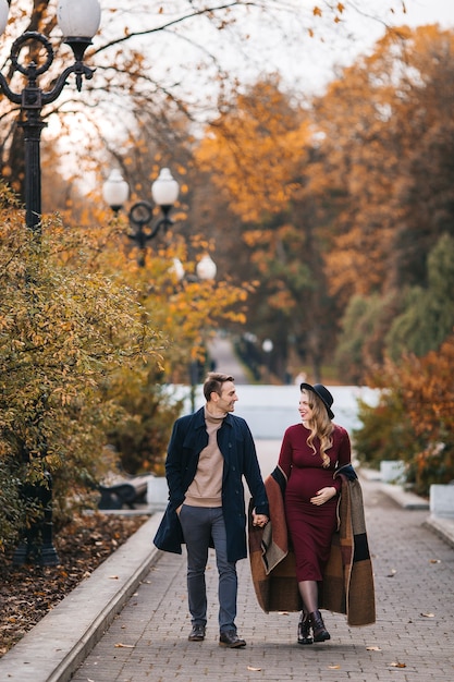 Young couple in love happy man and his pregnant wife holding hands and walking through a park on a s...