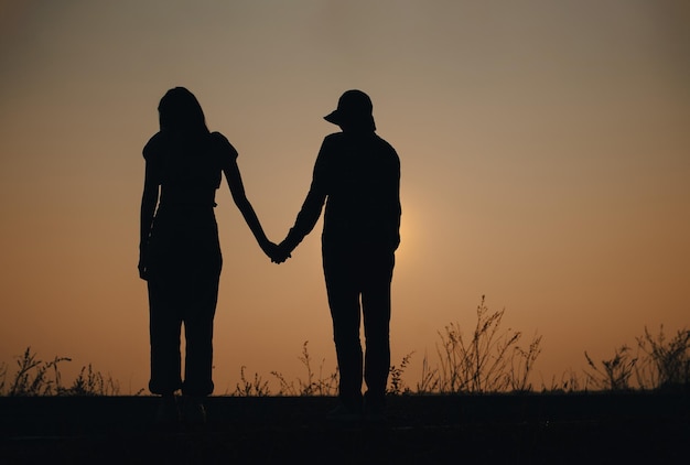 Giovane coppia innamorata che si tiene per mano guardando il tramonto