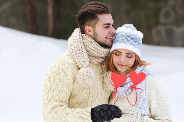 Young couple in love holding red paper hearts outdoors in winter