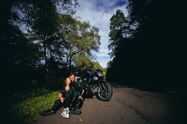 young couple in love hugging and kissing near a black sports motorcycle on the background of a forest road