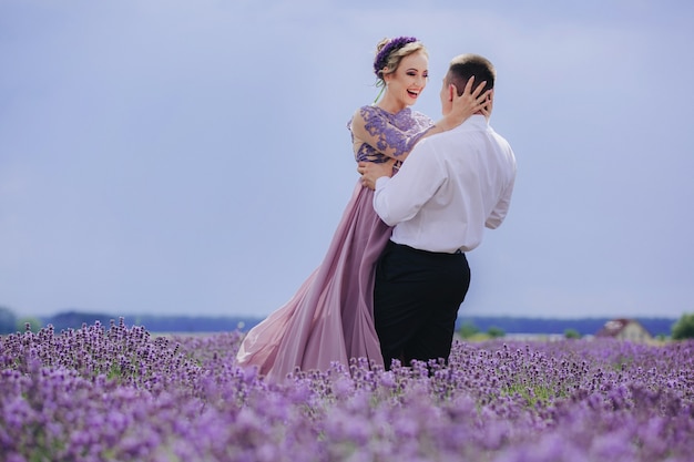 Giovani coppie nell'amore che abbracciano e camminano in un campo di lavanda in una giornata nuvolosa estiva