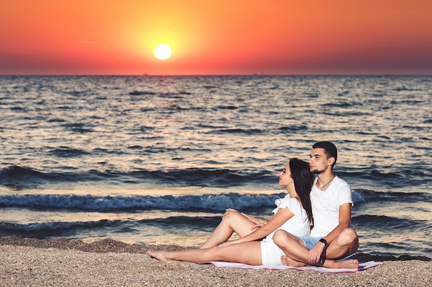 A young couple in love is resting and enjoying the sunrise at the seaside