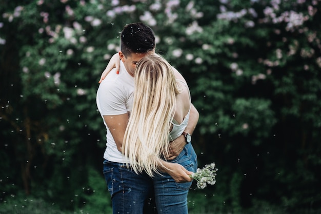 A young couple in love kissing in the park in front of a flowering bush